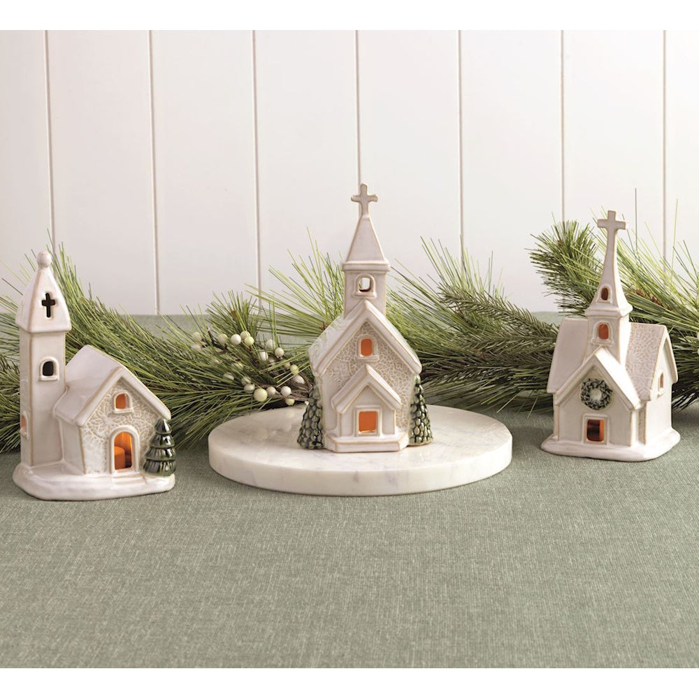 Three light-up white ceramic church figurines displayed with pine garland on a table.