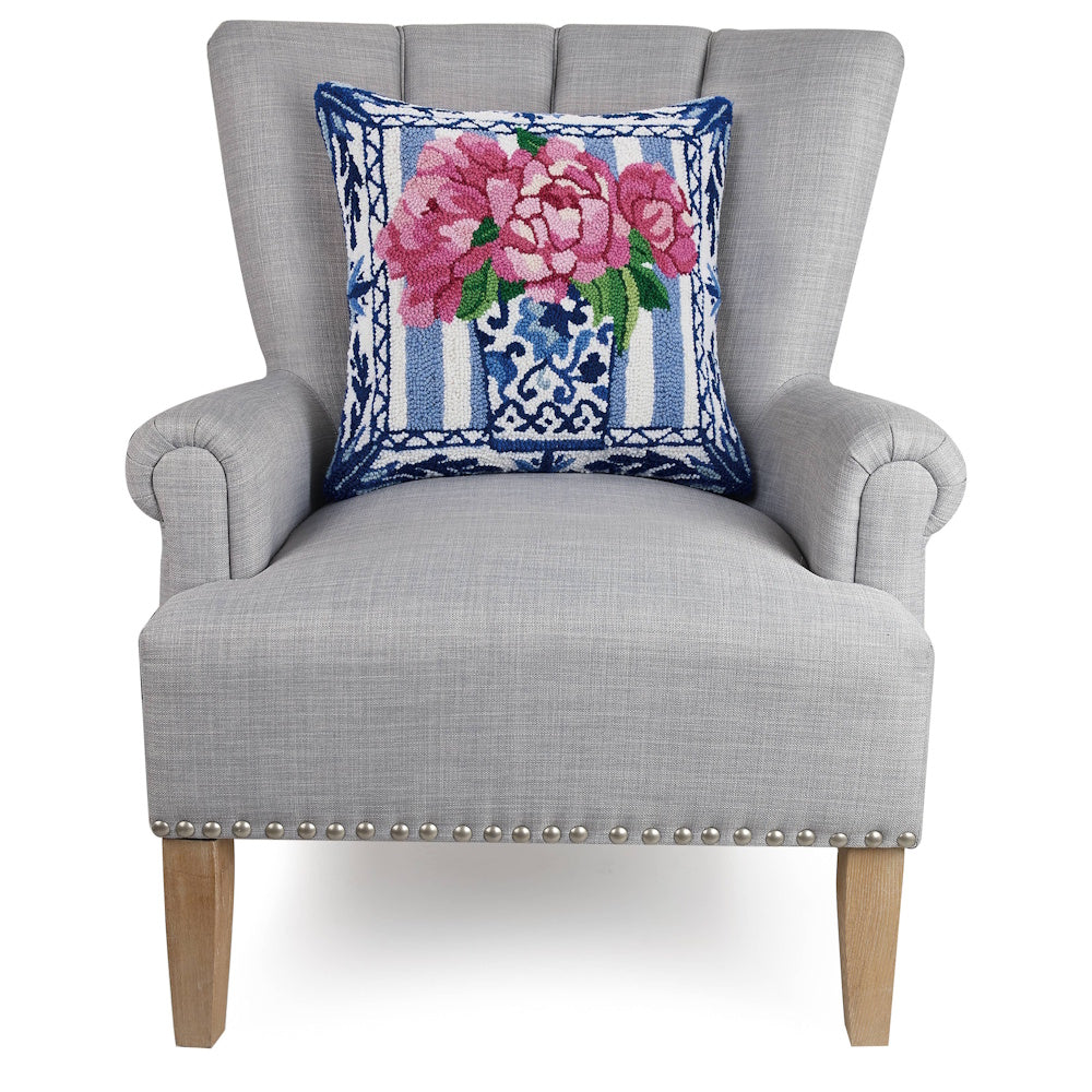 Grey armchair with a floral needlepoint pillow featuring pink peonies and a blue and white ginger jar.