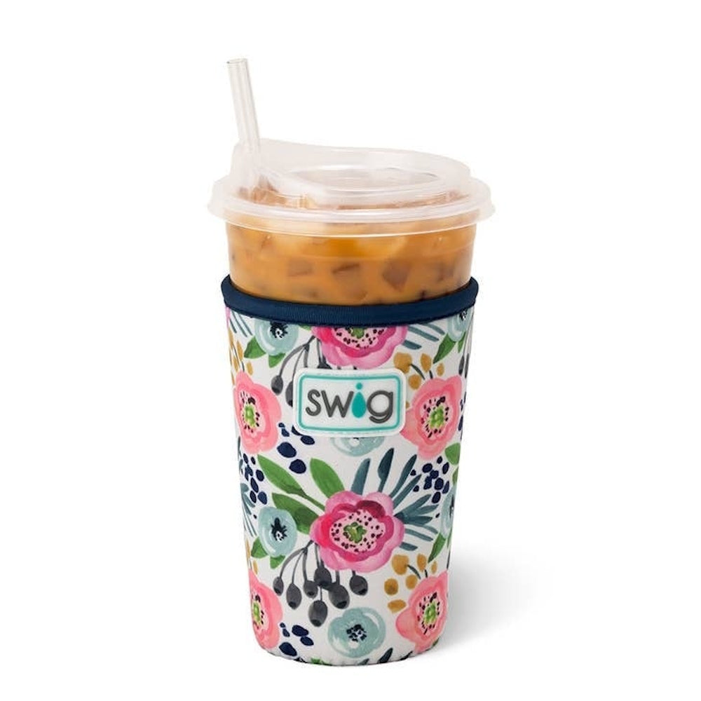 An iced coffee cup with a lid and straw, wrapped in a Swig brand floral-patterned sleeve.