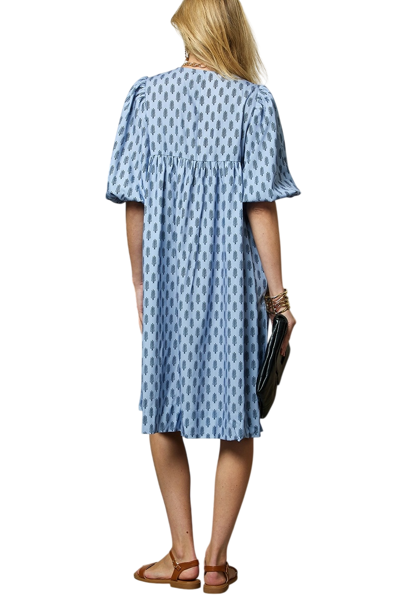 Woman from behind wearing a blue block-print midi dress with puff sleeves, brown sandals, and a clutch bag