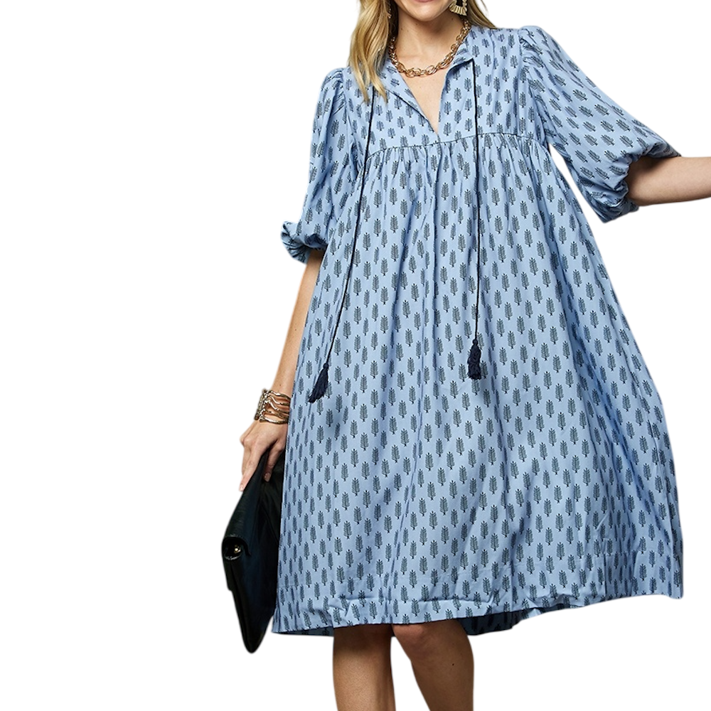 A woman wearing a light blue, knee-length babydoll dress with puff sleeves and a repeating dark leaf pattern.