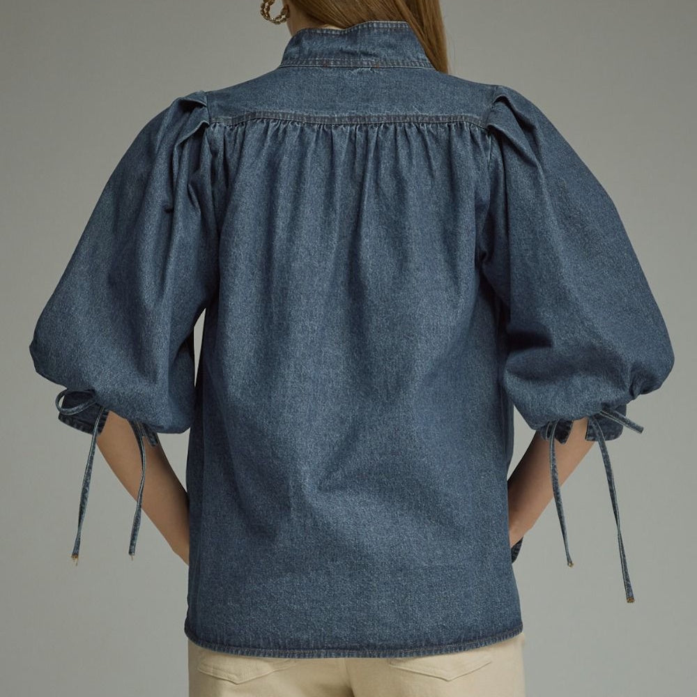 Back view of a dark blue denim top with gathered back yoke and tied puff sleeves.