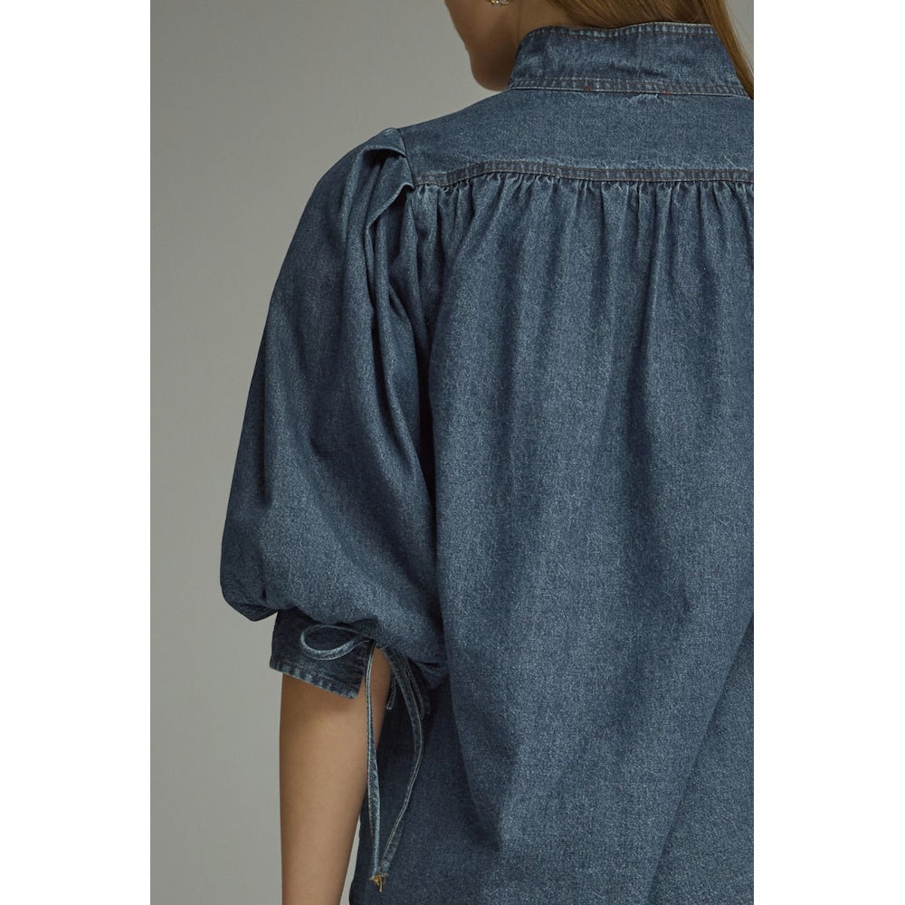 Close-up back view of a dark blue denim top showing a gathered back yoke and tied cuff detail.
