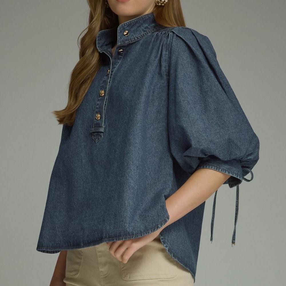 Three-quarter view of a dark blue denim top showing a button placket, high collar, and puff sleeve.