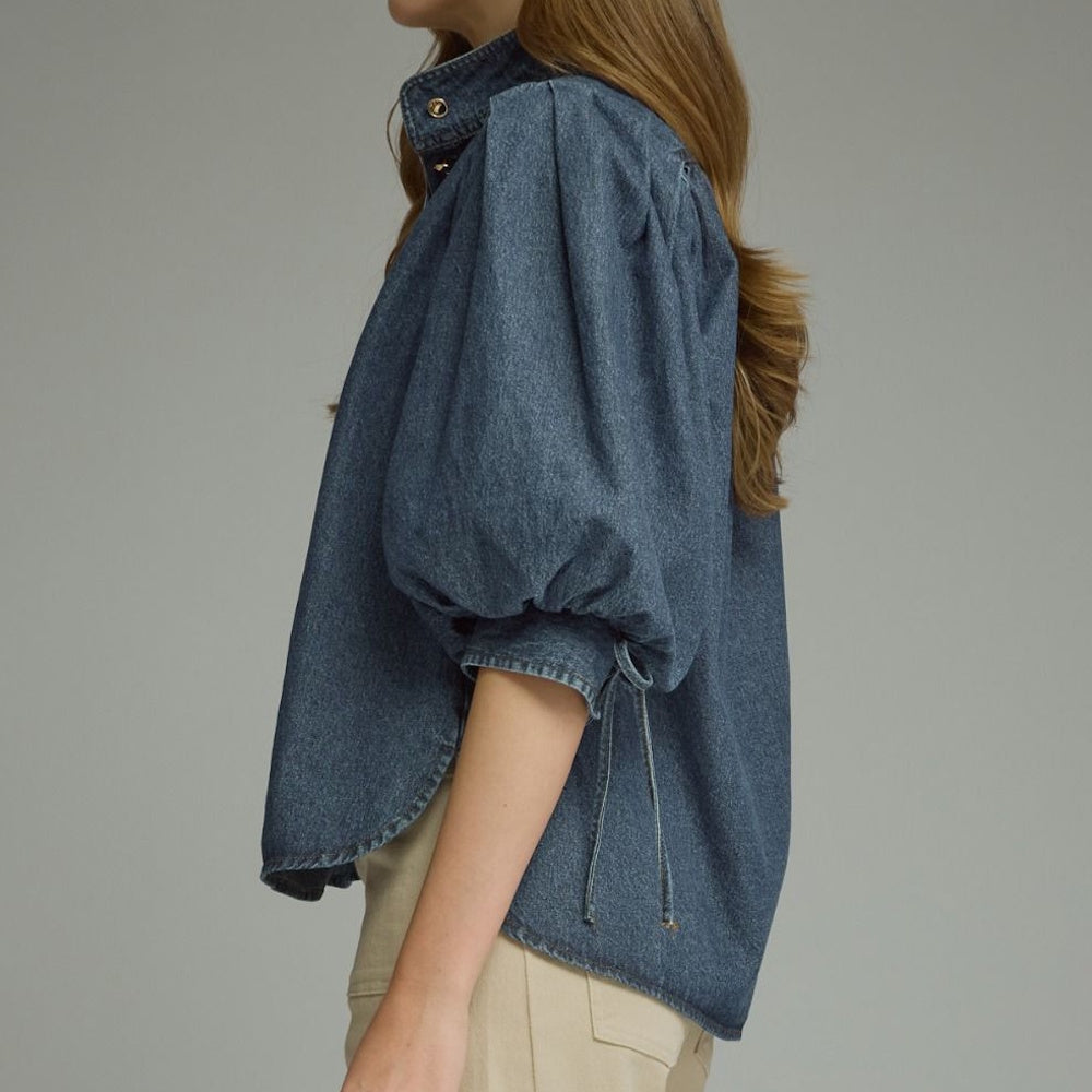 Side view of a dark blue denim top showing volume puff sleeves and high-low curved hem.