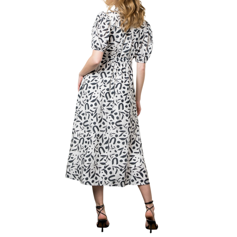 Back view of a woman in a black and white patterned maxi dress with puffed sleeves and black strappy heels.