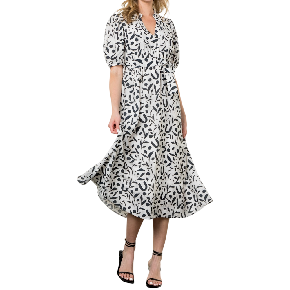 A woman wearing a black and white patterned midi dress with puff sleeves and strappy black heels.