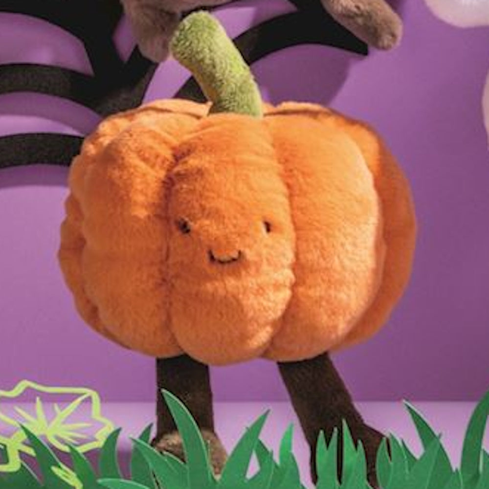 A plush orange pumpkin toy with a green stem, tiny smiling face, and brown legs stands on a purple background.