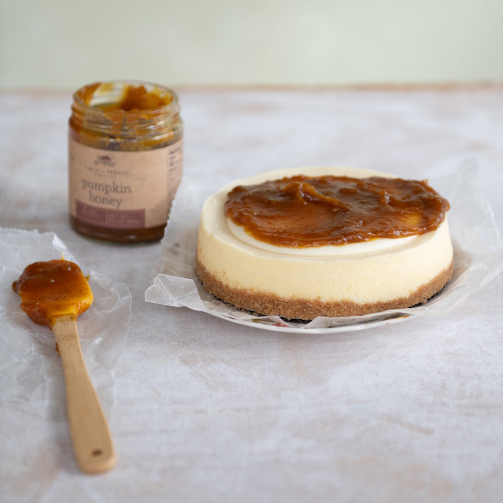A round cheesecake topped with pumpkin honey butter, next to a jar of the spread and a small wooden spatula.