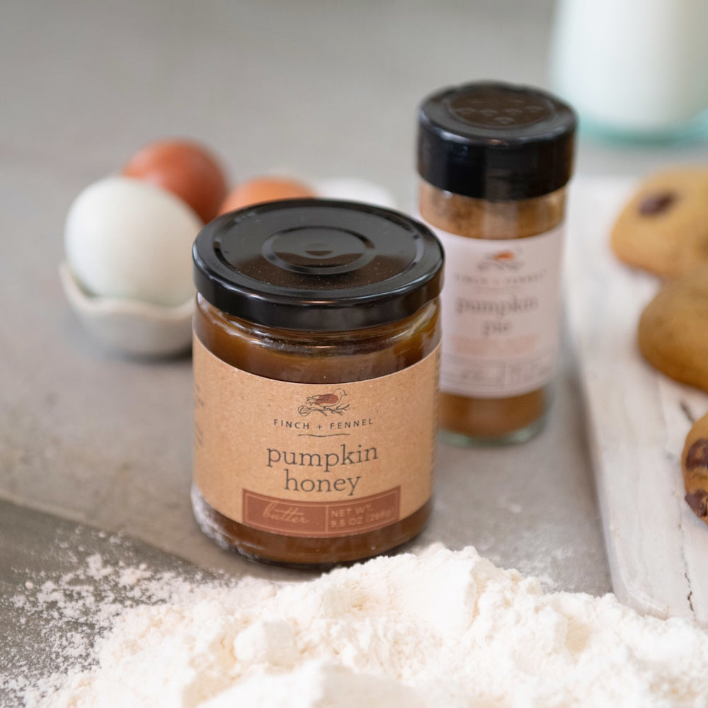 A jar of Finch & Fennel pumpkin honey butter sits by flour, a spice jar, cookies, and eggs.