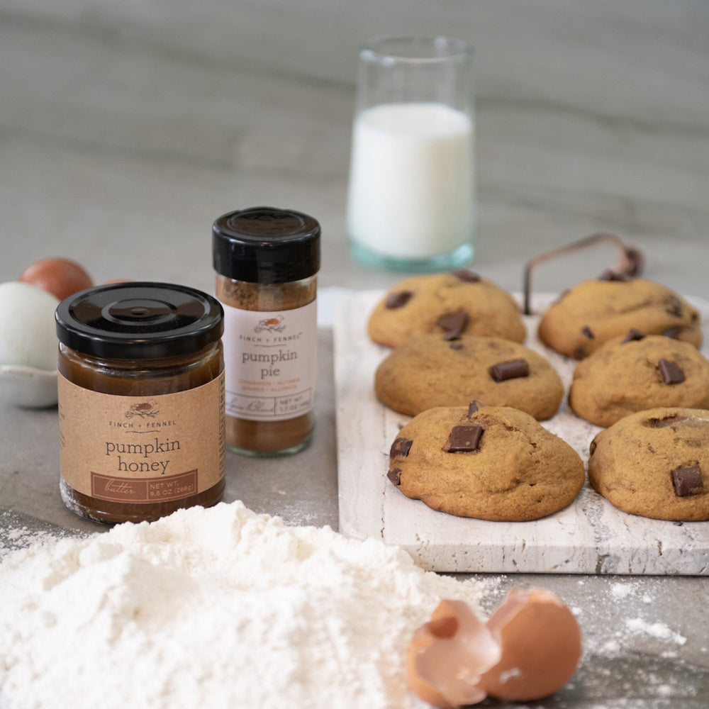 A jar of pumpkin honey butter next to spices, freshly baked cookies, flour, and a glass of milk.