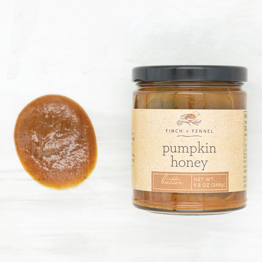 A glass jar of Finch + Fennel pumpkin honey butter with a black lid next to a small dollop of the spread.