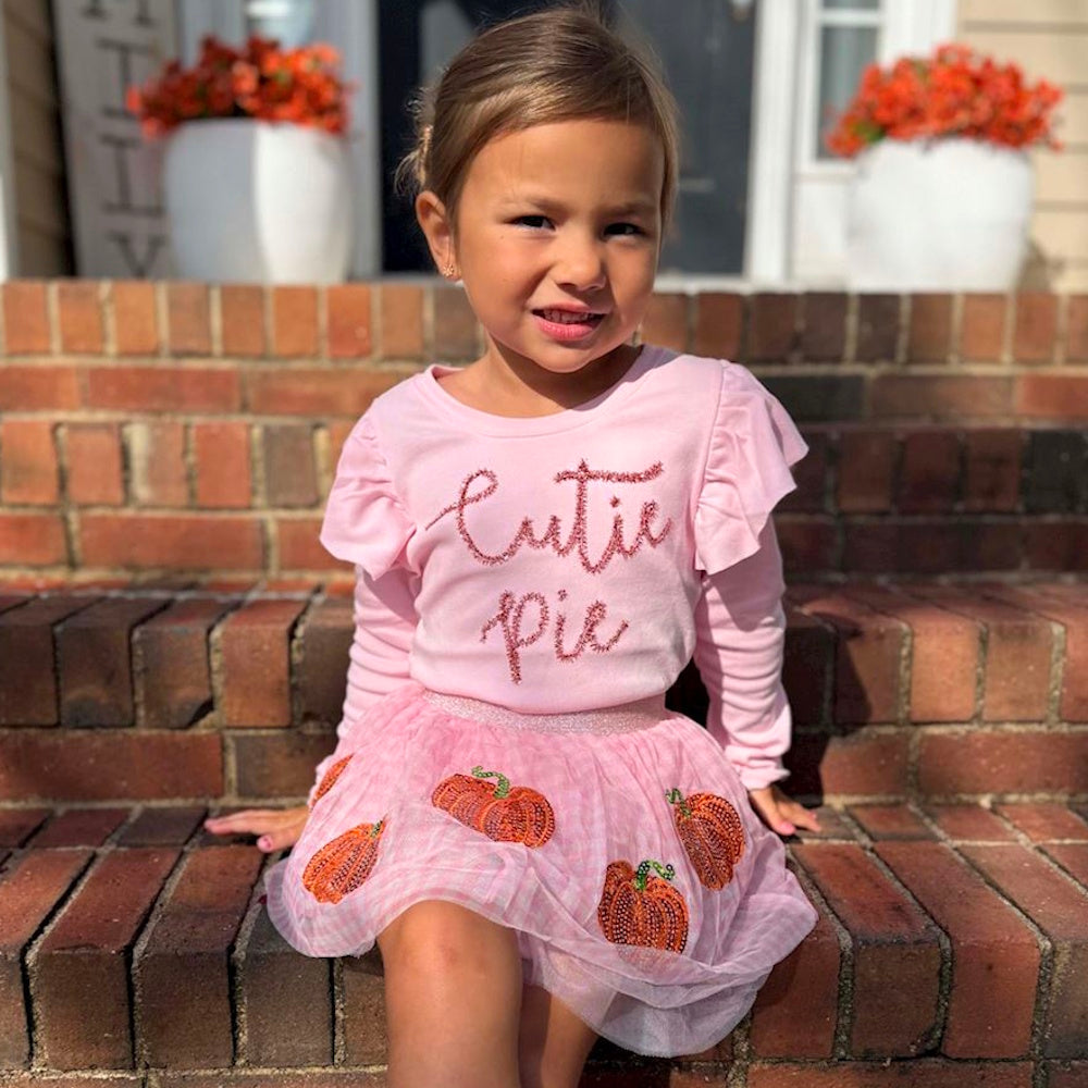 Toddler girl on brick steps wearing a pink 'Cutie pie' shirt and pink tulle sequin pumpkin skirt.