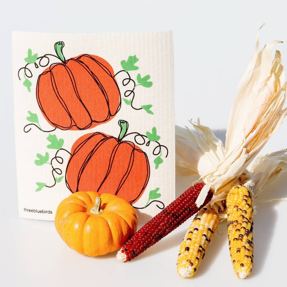 A pumpkin dishcloth styled with a real mini pumpkin and three ears of colorful Indian corn.