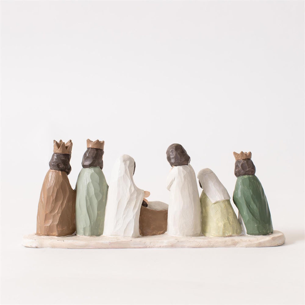 Back view of carved wooden Nativity scene figurines standing on a white base.