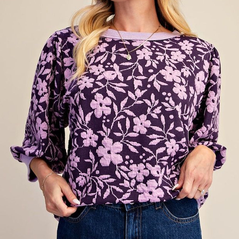 Woman wearing a dark purple floral long-sleeve top with light purple floral patterns and blue jeans.