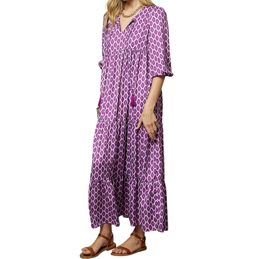 Woman in a purple geometric-print tiered maxi dress with puff sleeves, a v-neck with tassels, and sandals.