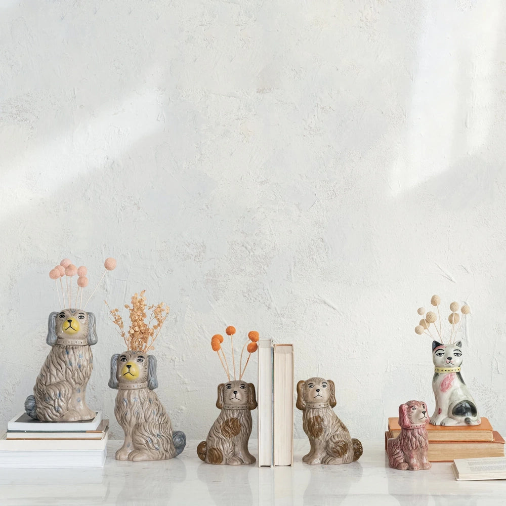 Ceramic spaniel dog and calico cat figurines used as vases and bookends with books on a white tabletop.