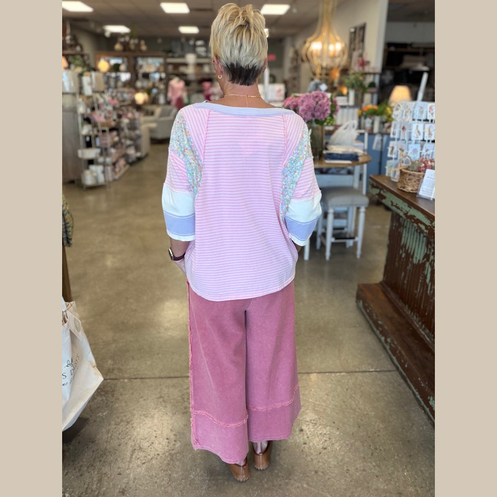 Back view of a woman wearing a pink striped mixed-print knit top and mauve mineral-washed wide-leg pants in a boutique.