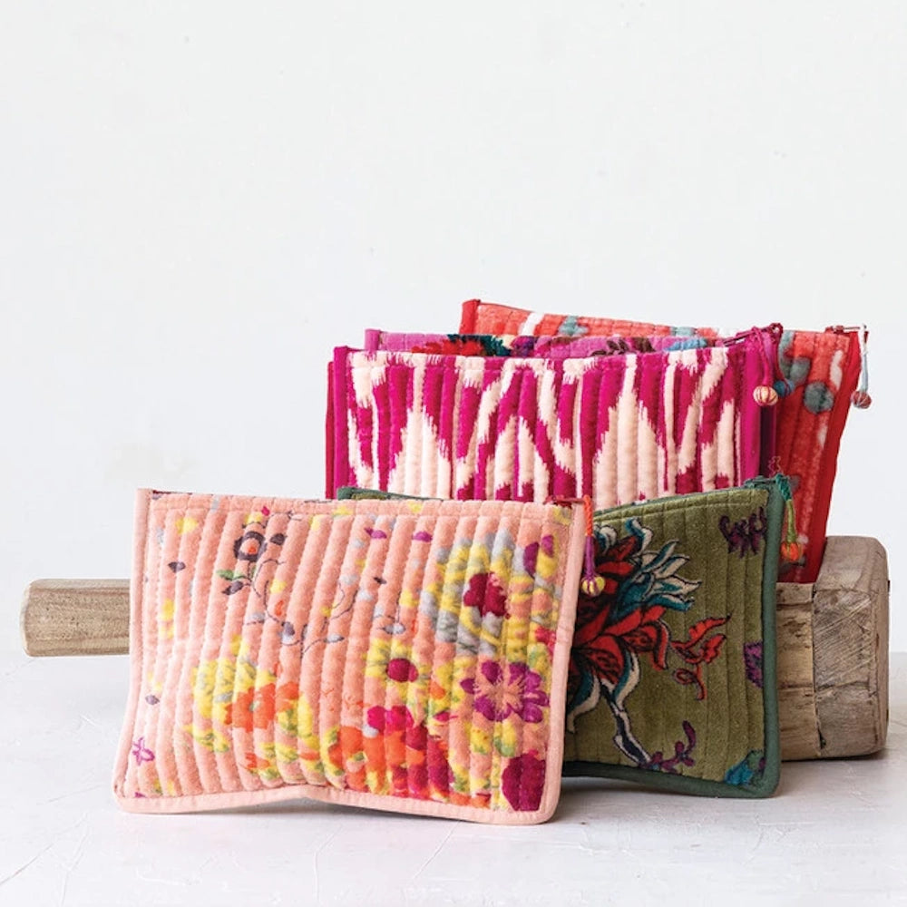 A collection of colorful quilted cotton velvet zip pouches with floral and ikat patterns resting against a wooden block.