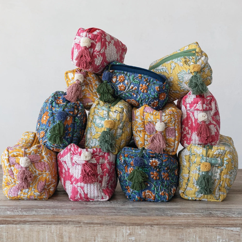 Stacked floral quilted cotton zip pouches in pink, yellow, and blue with decorative tassels for organized storage.