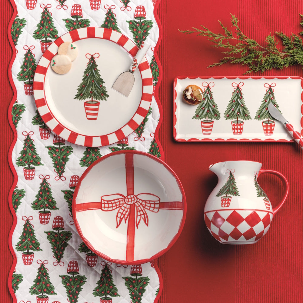Christmas table setting with a quilted tree runner, red-striped plates, bowl, pitcher, and tray.