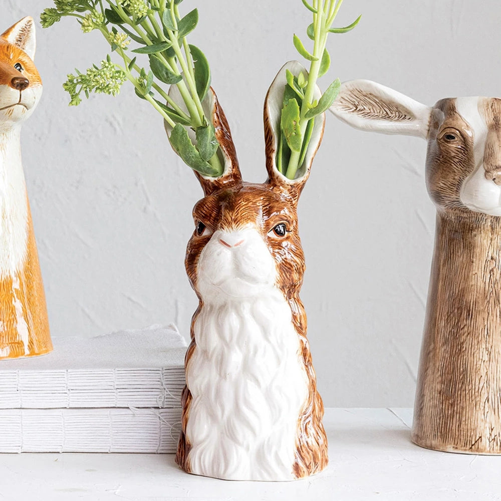Hand-painted stoneware rabbit bud vase with green sprigs in its ears, flanked by fox and goat vases.