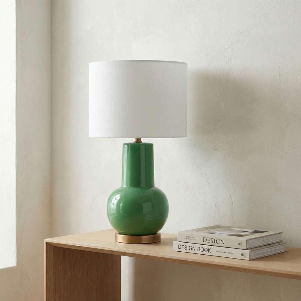 Green ceramic table lamp on a wooden console table alongside books, set against a neutral wall.