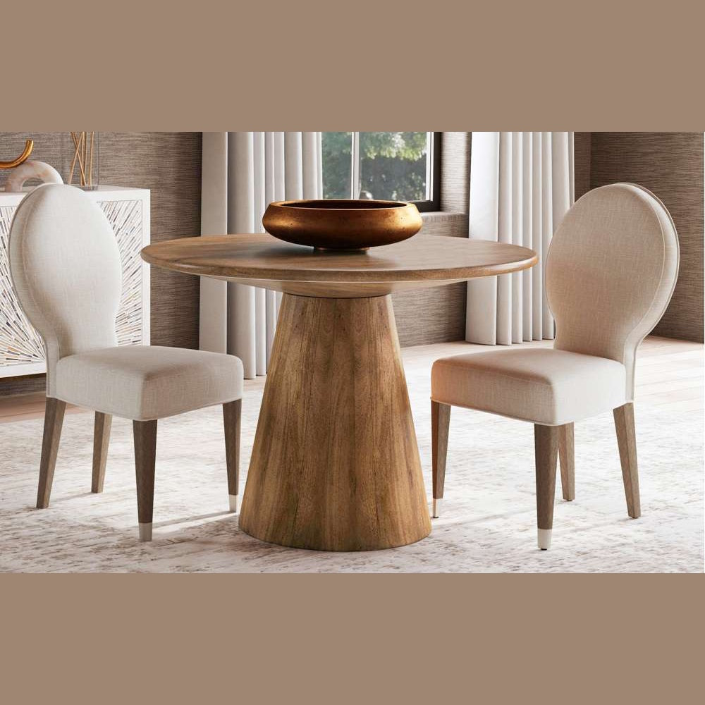 Modern round wood pedestal dining table with a bronze bowl and two cream upholstered chairs in a bright dining room.