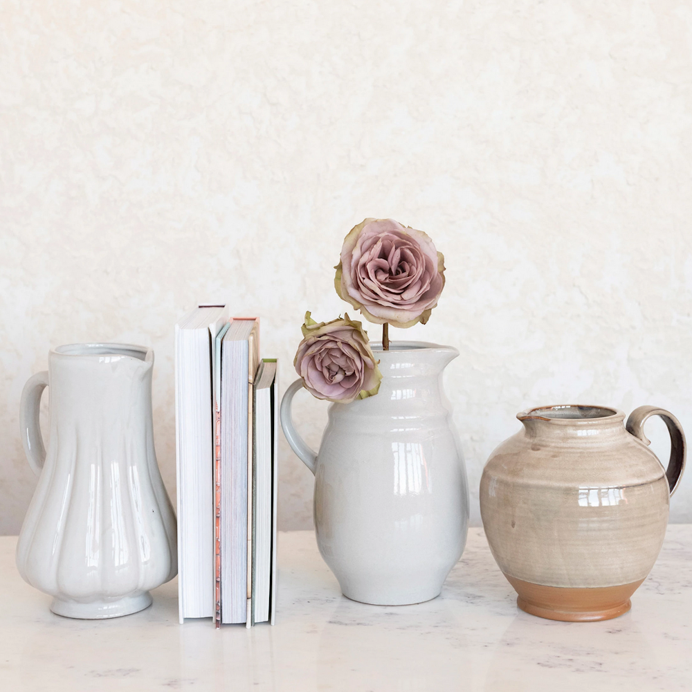Ceramic pitchers and books displayed on a surface, with mauve roses in the center pitcher.