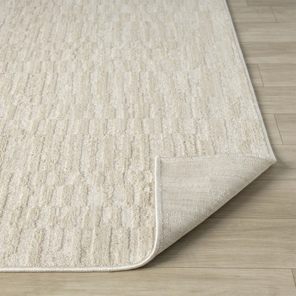 Close up of cream area rug corner showing textured geometric pattern, bound edges and durable backing material.