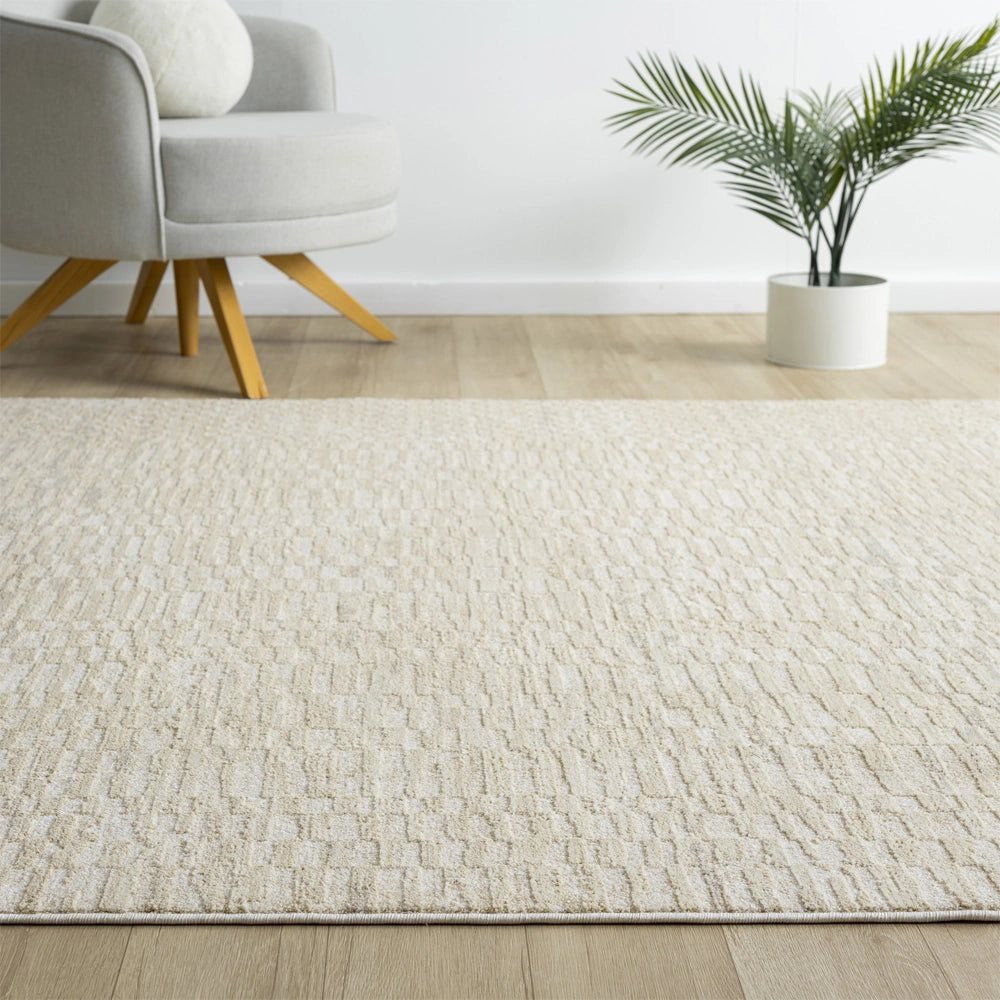 Close up of ivory textured area rug with geometric pattern in a modern room with armchair and potted plant.
