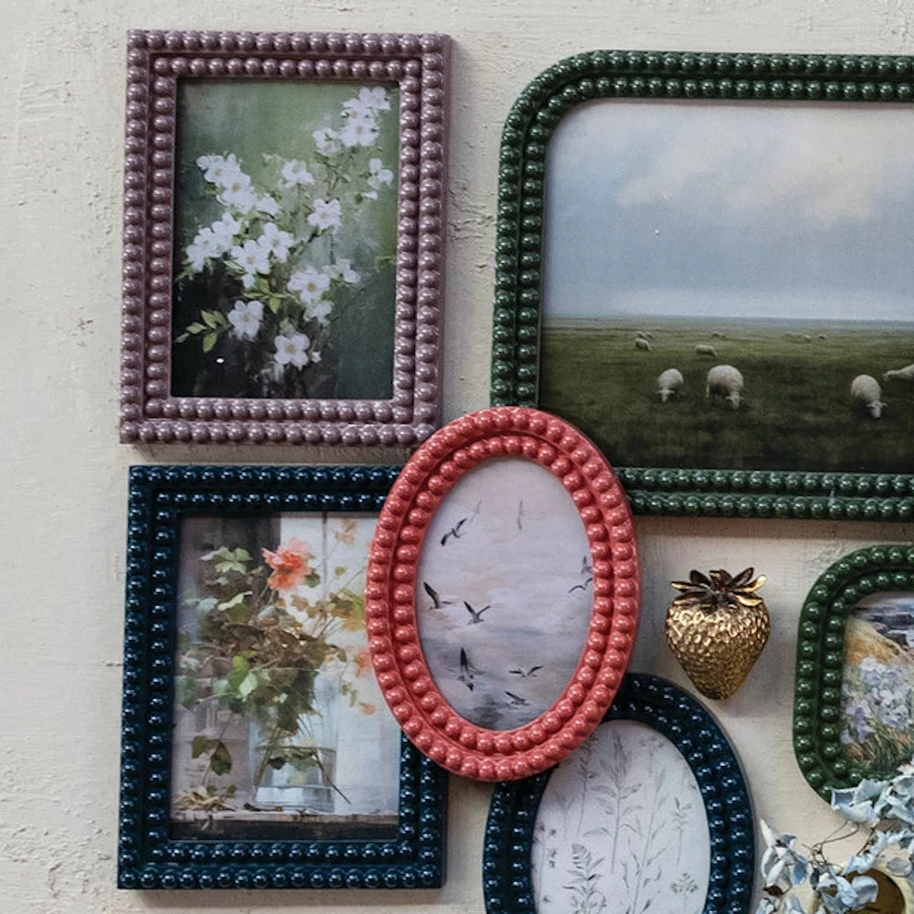 Beaded frames in various colors and shapes holding vintage-style botanical, landscape, and animal art on a beige wall.
