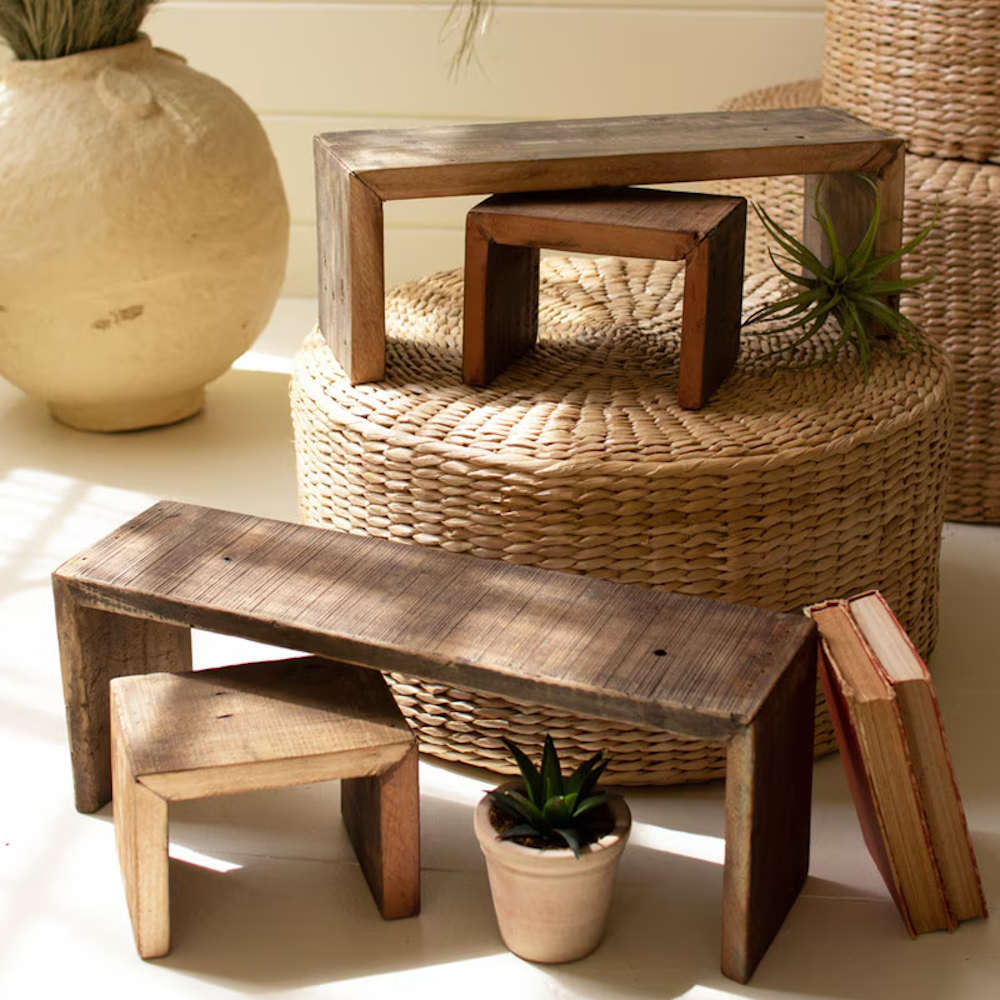 Rustic, recycled wood nesting risers in various sizes displayed on and around a woven pouf.