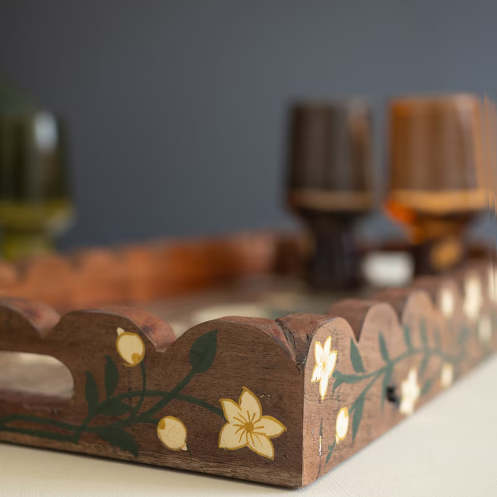 Detailed corner shot of a scalloped wooden tray with hand-painted white floral and leaf patterns.