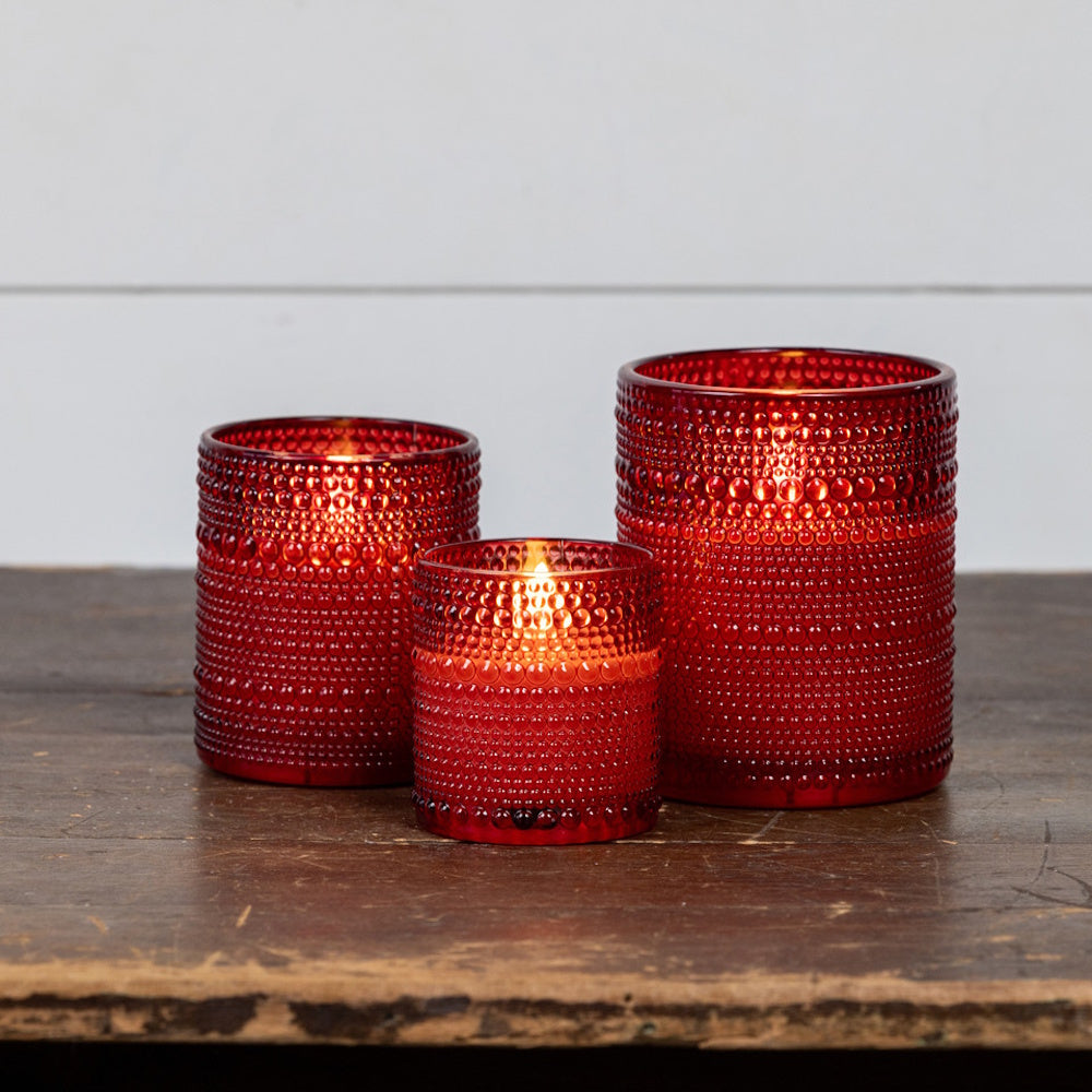 Set of three glowing flameless candles in red beaded glass holders sitting on a wooden surface.