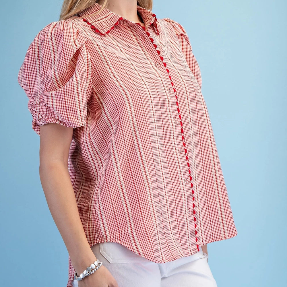 Woman in a red gingham button-down shirt with puff sleeves, ric-rac trim, and embroidery against a blue background.