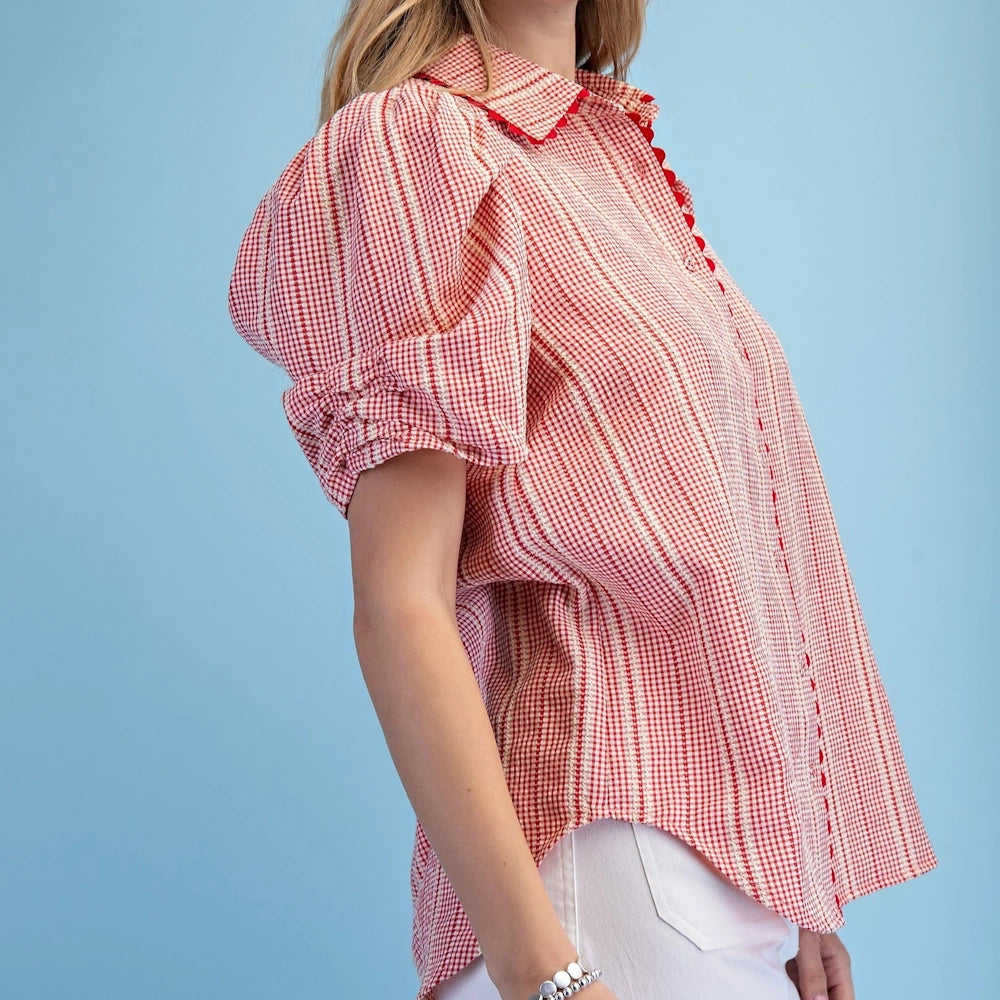 Side view of a woman in a red gingham button-down shirt featuring gathered puff sleeves and red ric-rac trim.