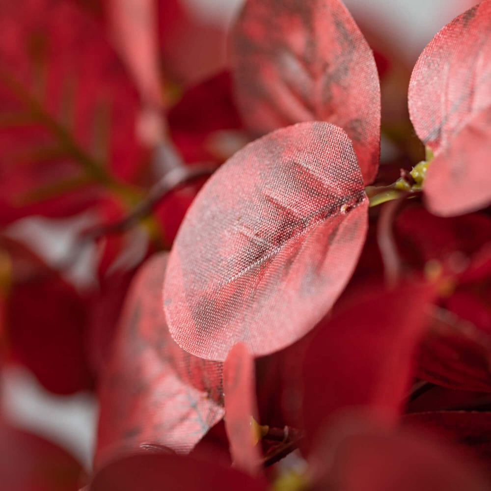 Close-up of red artificial eucalyptus leaves with detailed fabric texture and fine veins.