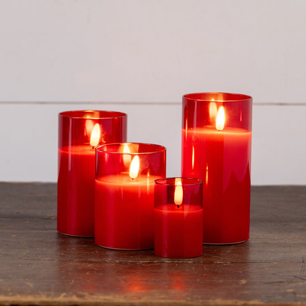 Four red glass flameless candles of varying sizes glowing on a dark wooden surface.