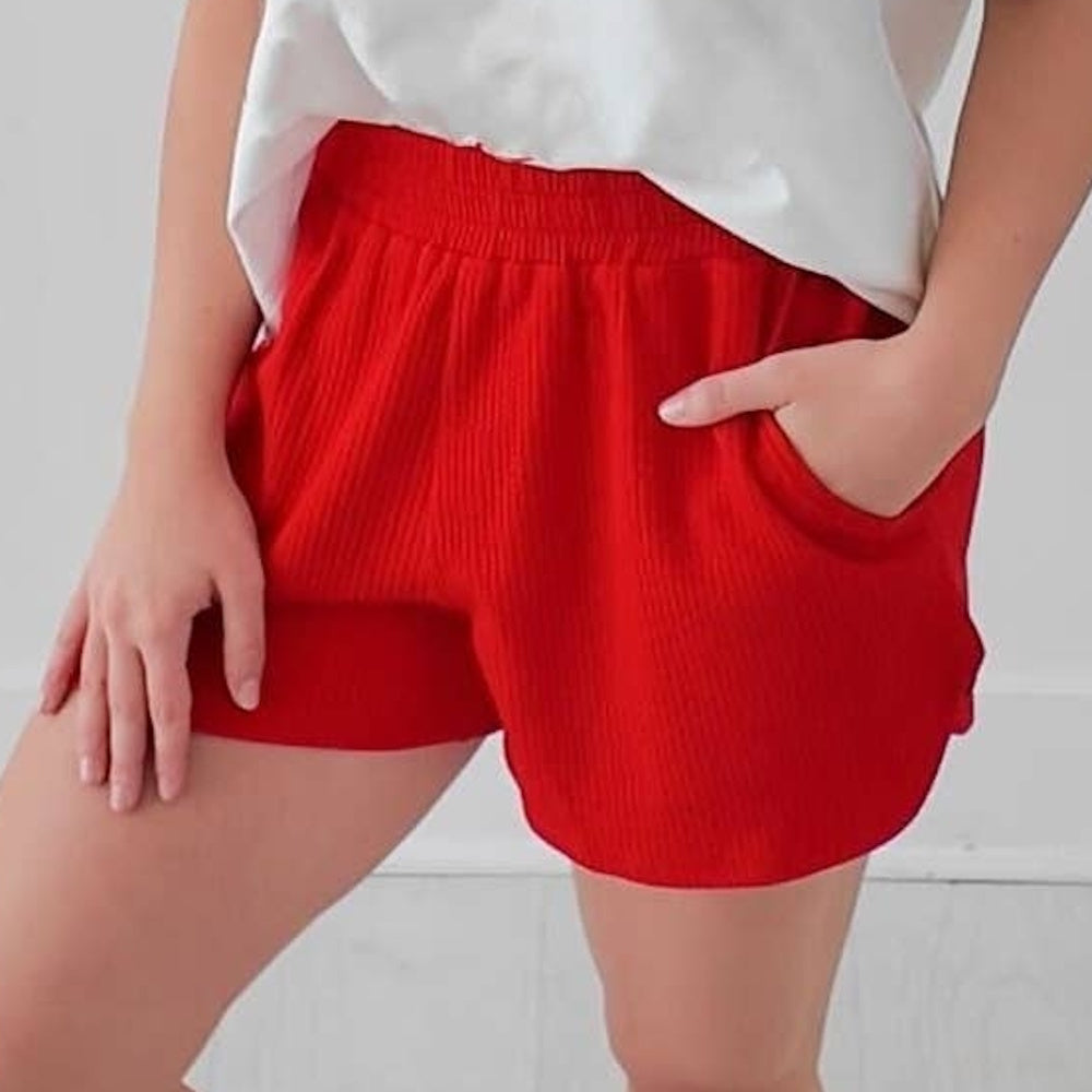 A person wearing bright red, textured knit shorts with side pockets and an elastic waistband.