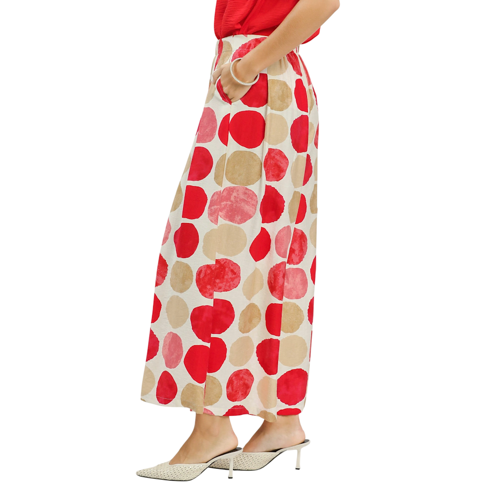 A person wearing wide-leg white pants with large red and tan polka dots, paired with pointed-toe heels.