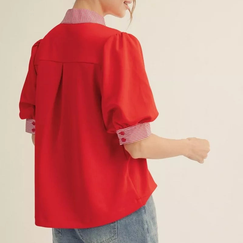 A person wearing a red short-sleeve blouse with puff sleeves and red-and-white striped collar and cuffs.