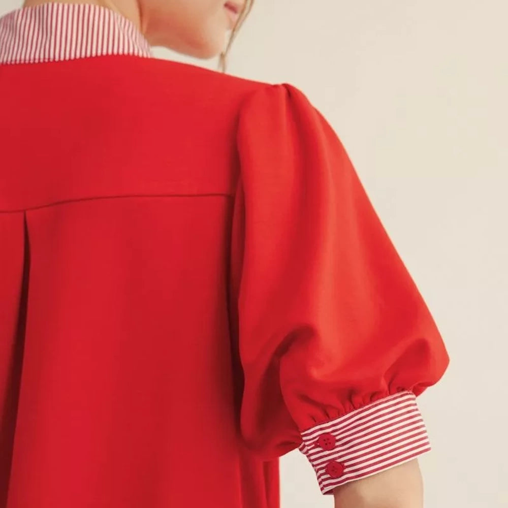 Close-up of a red blouse featuring a puff sleeve and red and white striped cuffs and collar.