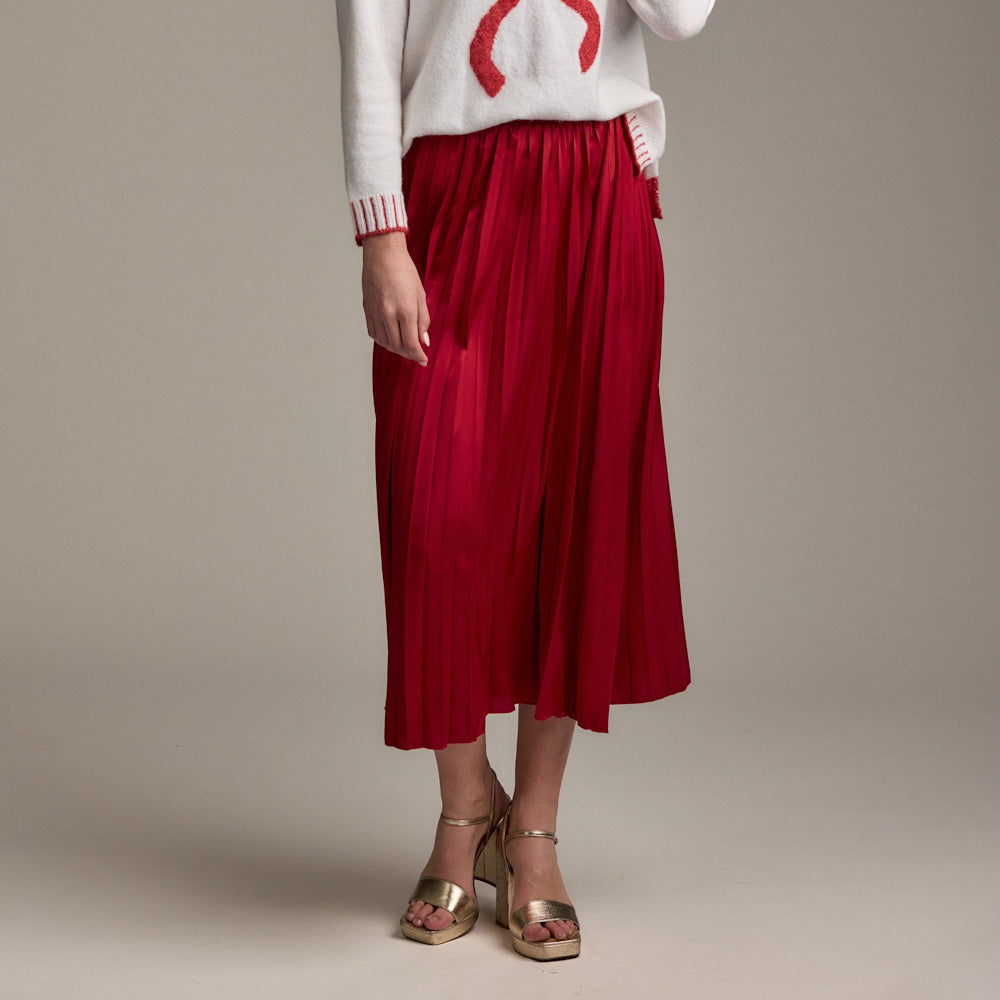 Model wearing a red Townes pleated midi skirt with a white graphic sweater and gold platform sandals.