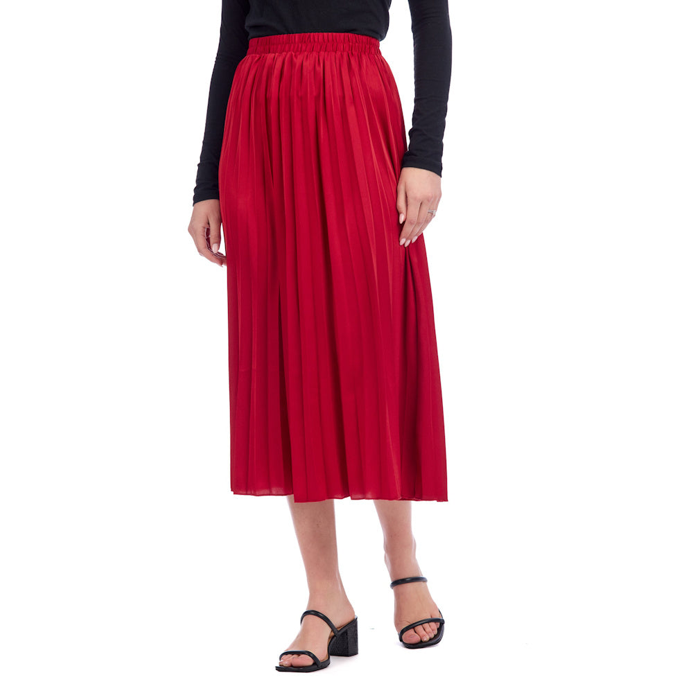 A person wearing a vibrant red Townes pleated midi skirt with a black long-sleeve top and black strappy heels.