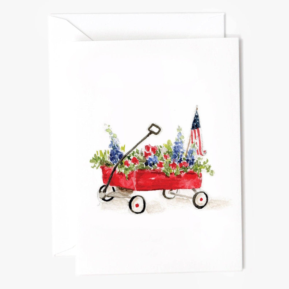 Watercolor illustration of a red wagon filled with blue and red flowers and a small American flag.