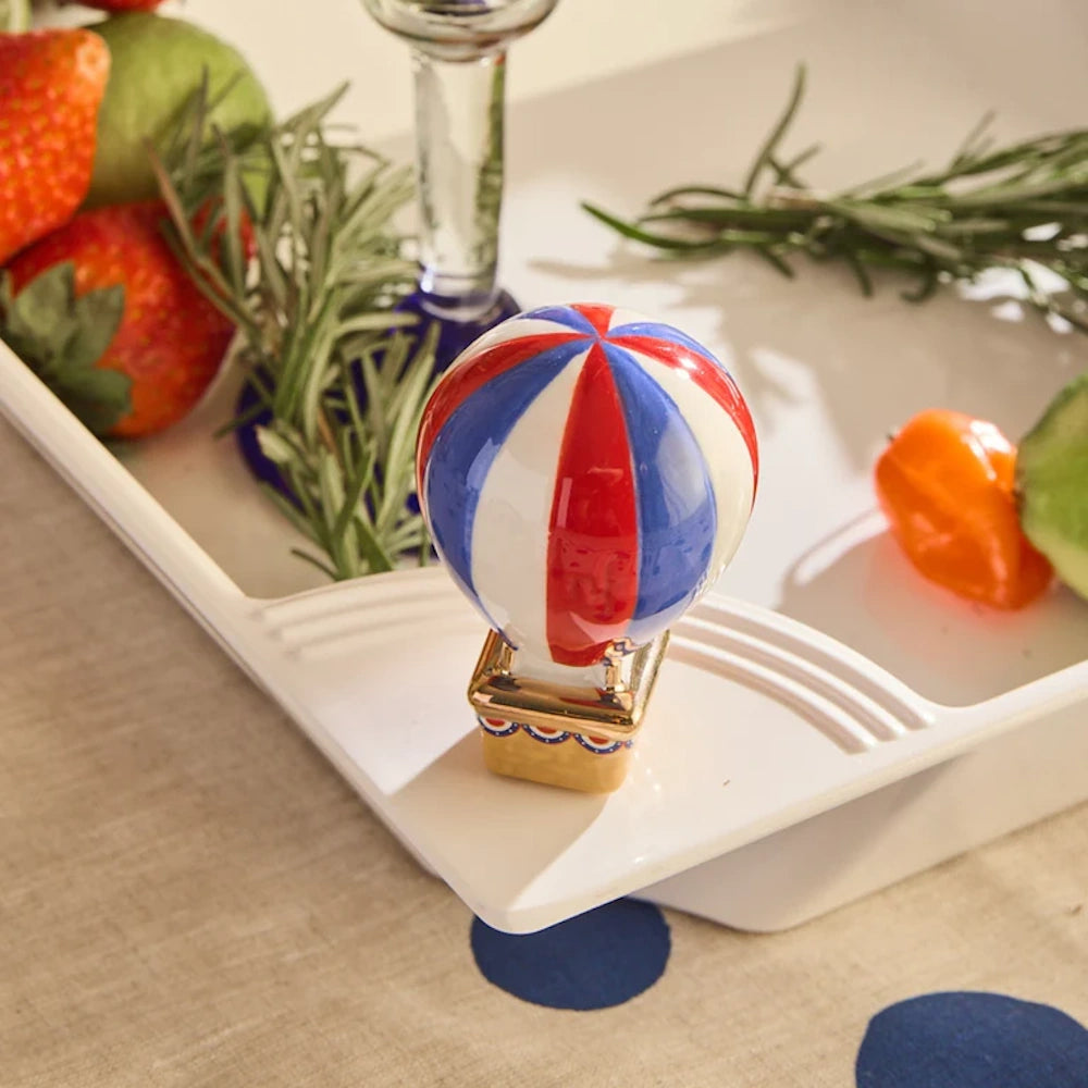 Red, white, and blue striped ceramic hot air balloon decorative accent on a tray near fresh fruit and herbs.