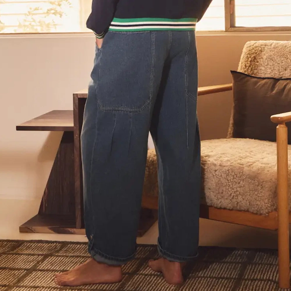 Person wearing relaxed-fit blue denim pants with large back pockets and cuffed hems, standing on a textured rug.