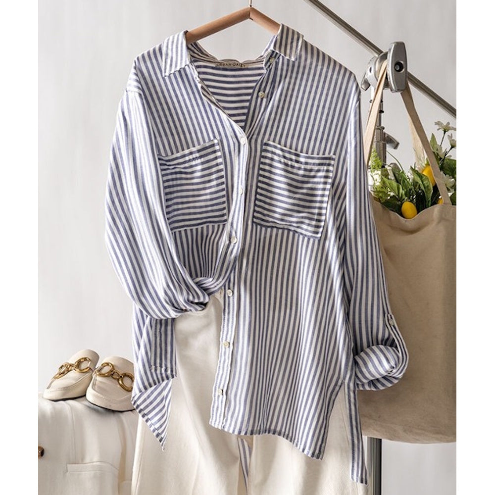 A relaxed-fit, blue and white vertical striped button-down shirt hanging above white trousers.
